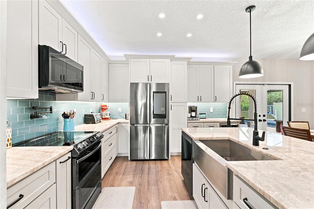A modern kitchen features white cabinets, stainless steel appliances, a farmhouse sink, and blue backsplash — 48 MISSION OAK COURT, ST AUGUSTINE, FL