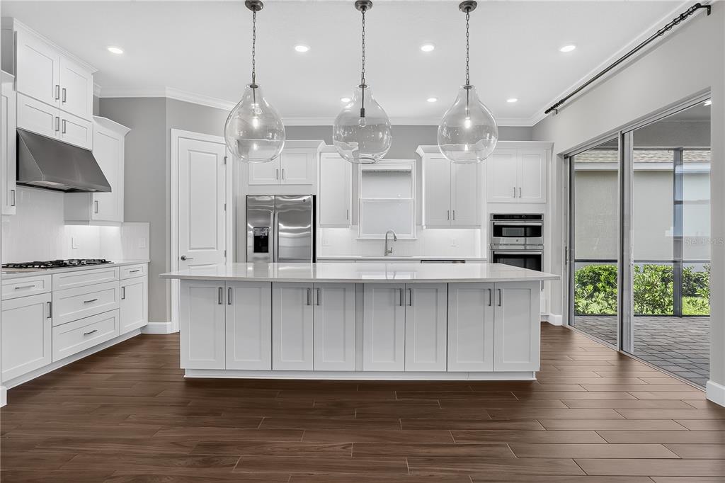 A modern kitchen features white cabinetry, a large central island, and dark wood-look flooring — 936 ARBOR GREEN TRAIL, ST CLOUD, FL