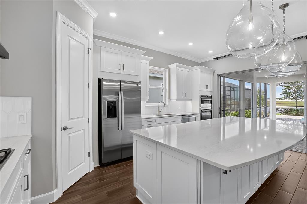 A modern kitchen features white cabinetry, a large quartz island, stainless appliances, and wood flooring — 936 ARBOR GREEN TRAIL, ST CLOUD, FL
