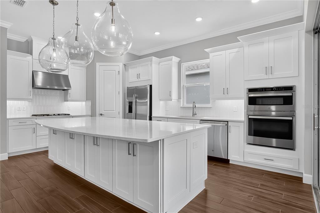 A modern kitchen features white cabinetry, a large center island, and stainless steel appliances — 936 ARBOR GREEN TRAIL, ST CLOUD, FL