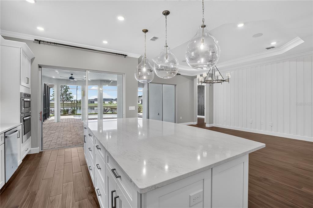 A kitchen island with white cabinets and quartz countertops sits before a sliding glass door — 936 ARBOR GREEN TRAIL, ST CLOUD, FL