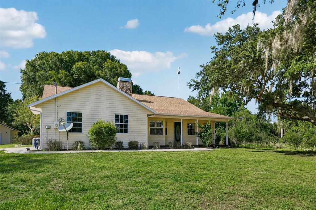 A single-story house with light-colored siding, a stone chimney, and a covered front porch — 204 JEFFERSON DRIVE, LAKE PLACID, FL