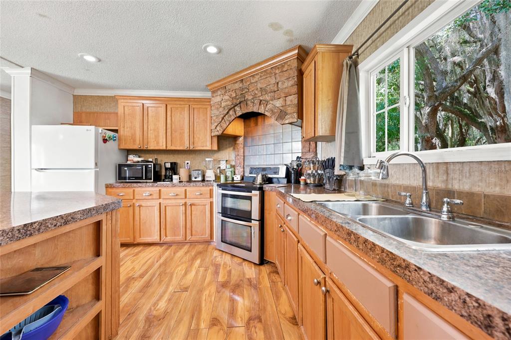 A kitchen features wood cabinets, stone-accented range hood, stainless steel appliances, and a double sink — 1837 STATE ROAD 20, HAWTHORNE, FL