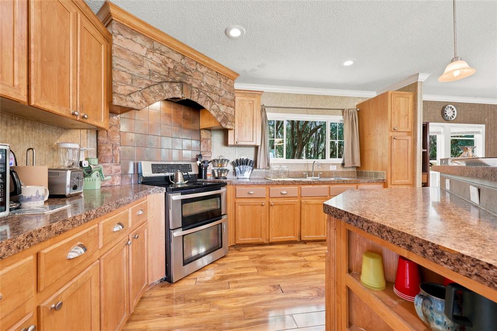 A kitchen features wood cabinets, stone backsplash, stainless steel appliances, and a granite-topped island — 1837 STATE ROAD 20, HAWTHORNE, FL