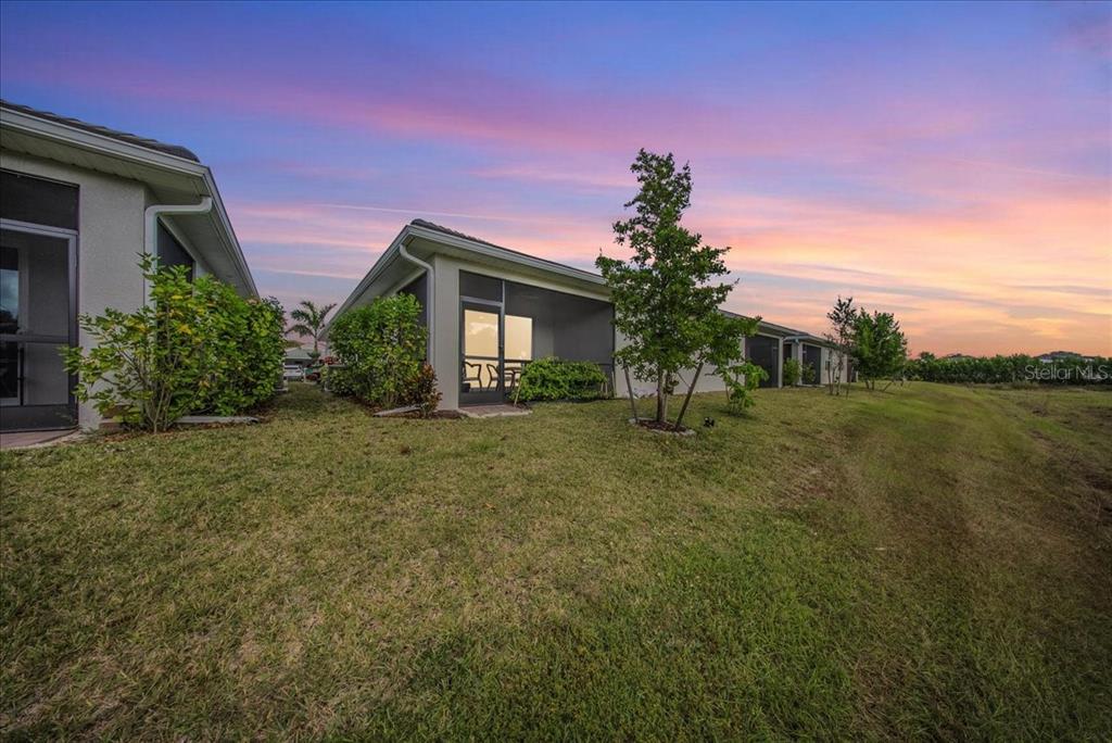 A view of the exterior of a suburban house with a screened-in patio at sunset — 1074 ENBROOK LOOP, NAPLES, FL