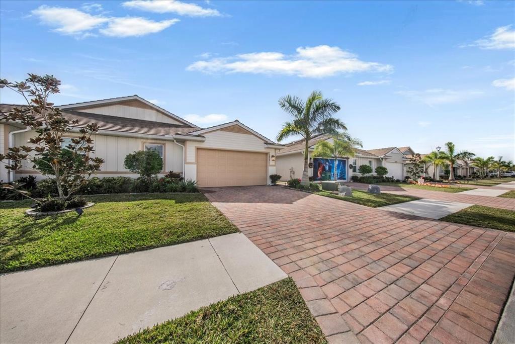 A single-story house with a tan garage, brick paver driveway, and palm trees in front — 1074 ENBROOK LOOP, NAPLES, FL