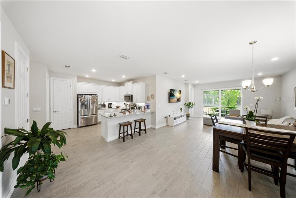 An open-concept kitchen and living area featuring white cabinetry, wood-look tile flooring, and dining space — 1074 ENBROOK LOOP, NAPLES, FL
