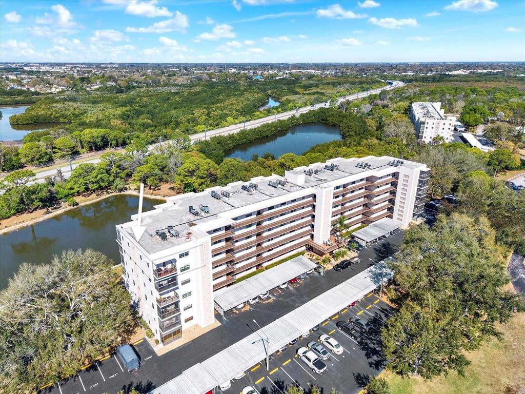 An aerial view shows a multi-story apartment building with a parking lot and pond — 8186 TERRACE GARDEN DRIVE N UNIT 601, ST PETERSBURG, FL