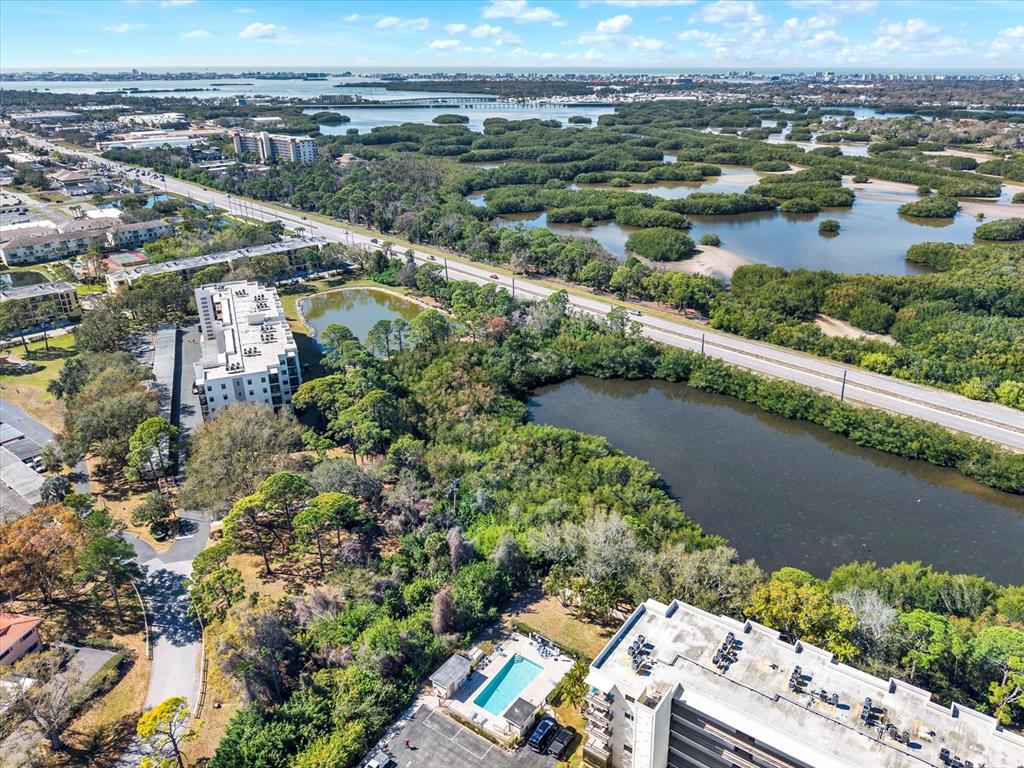 An aerial view shows apartment buildings, a swimming pool, ponds, and a highway near wetlands — 8186 TERRACE GARDEN DRIVE N UNIT 601, ST PETERSBURG, FL