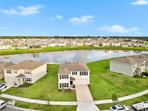 An aerial view shows two suburban houses situated on a grassy lot beside a pond — 16636 WINDMILL FORGE PASS, WIMAUMA, FL