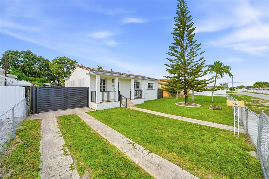 A white single-story house with a front porch, concrete driveway, and a tall pine tree — 465 E 38TH STREET, HIALEAH, FL