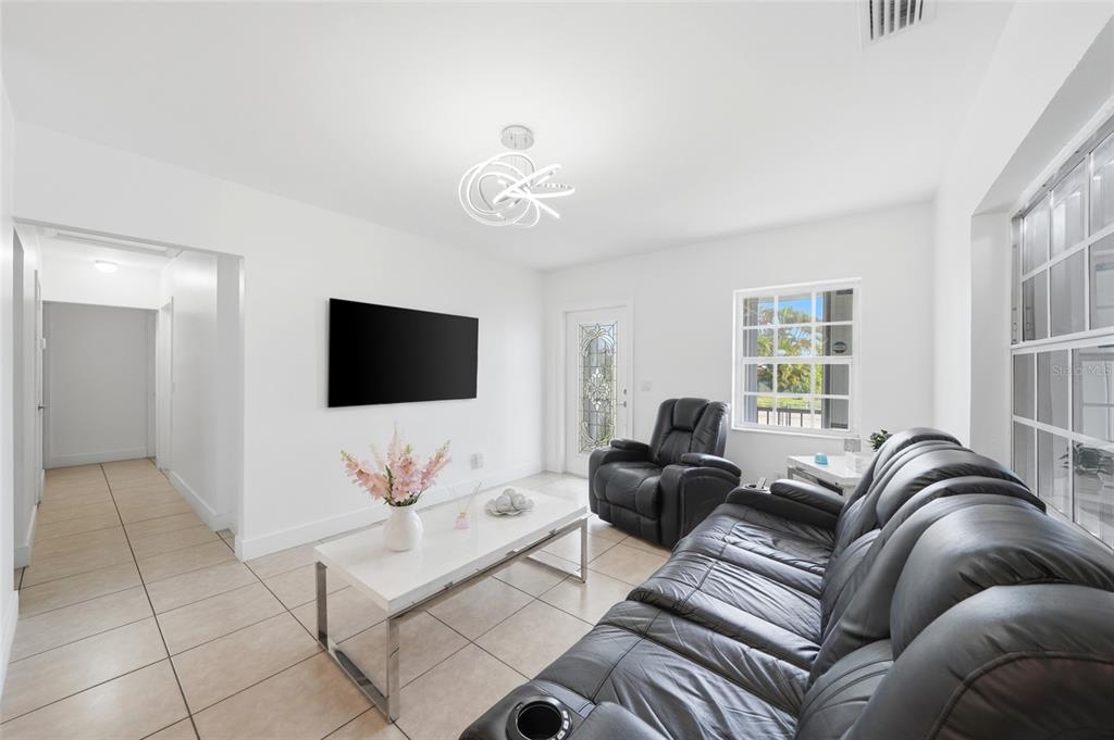 A living room features white walls, tile flooring, a black leather sofa, and a television — 465 E 38TH STREET, HIALEAH, FL