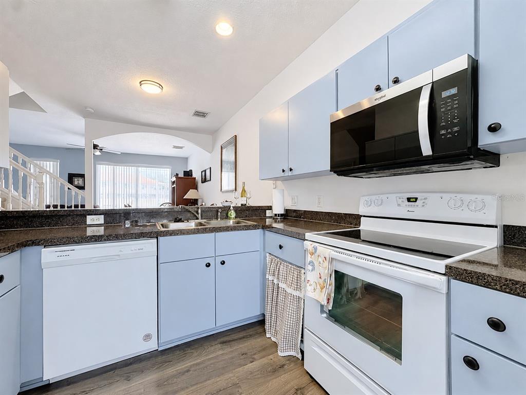 A kitchen with wood cabinets, dark granite countertops, stainless steel appliances, and a pass-through window — 1201 S BEACH CIR, KISSIMMEE, FL