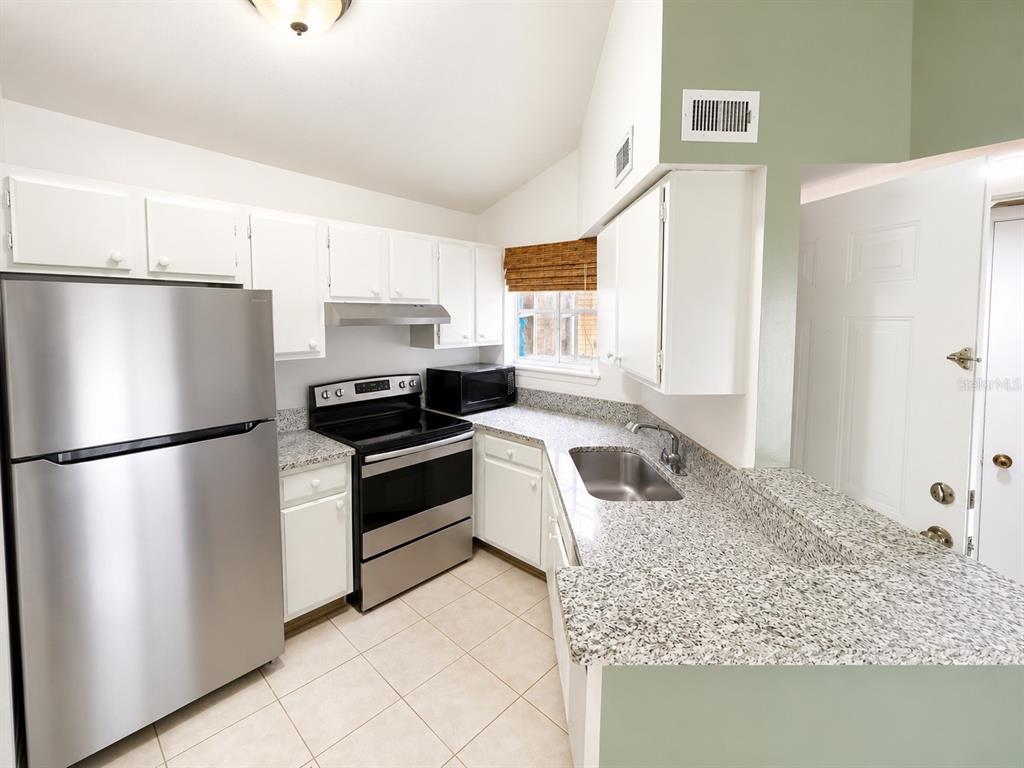 A kitchen features white cabinets, granite countertops, stainless steel appliances, and light-colored tile flooring — 1908 LAKE ATRIUMS CIRCLE UNIT 0, ORLANDO, FL