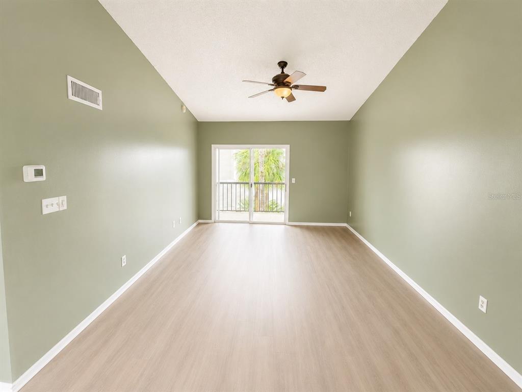 An empty living room features sage green walls, light wood-look flooring, and a sliding glass door — 1908 LAKE ATRIUMS CIRCLE UNIT 0, ORLANDO, FL