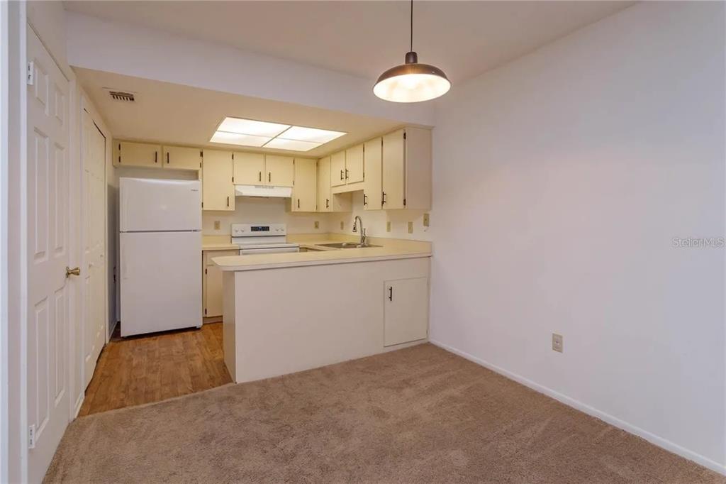 A kitchen with white cabinets and appliances features a breakfast bar overlooking a carpeted area — 68 WINDTREE LANE UNIT 201, WINTER GARDEN, FL
