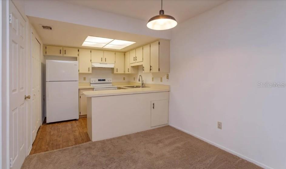 A kitchen with white cabinets and appliances features a breakfast bar overlooking a carpeted area — 68 WINDTREE LANE UNIT 201, WINTER GARDEN, FL