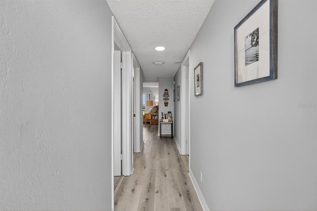 A hallway with light gray walls, wood-look flooring, and recessed lighting leads to a room — 2700 OCEAN SHORE BOULEVARD UNIT 114, ORMOND BEACH, FL
