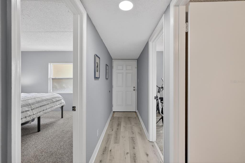 A hallway with light wood-look flooring leads to a white door between two rooms — 2700 OCEAN SHORE BOULEVARD UNIT 114, ORMOND BEACH, FL