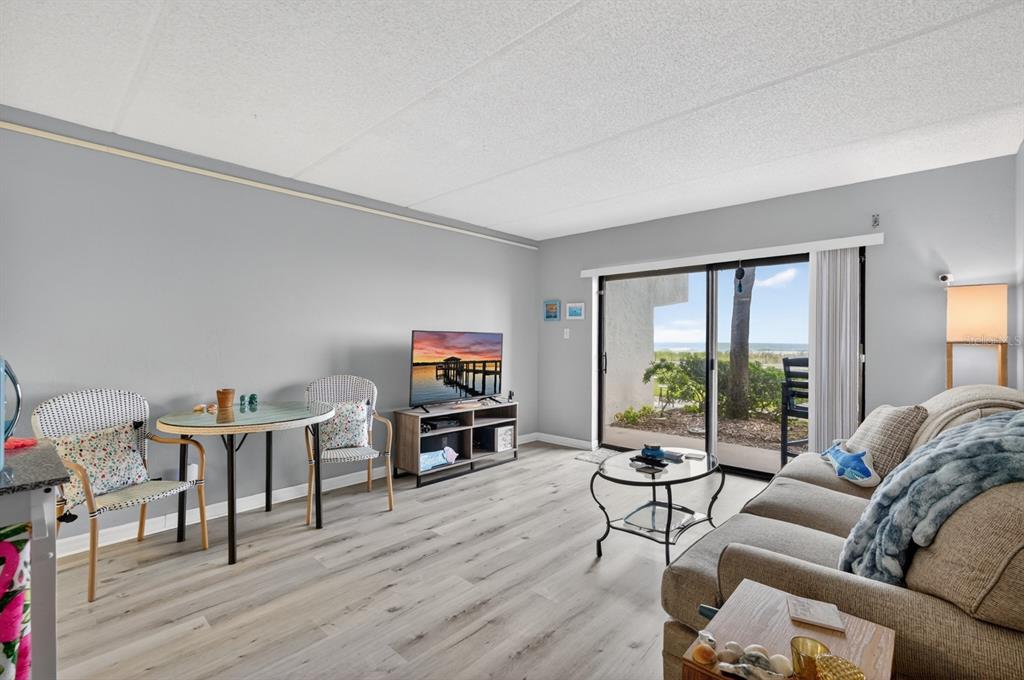 A living room with light wood floors, a sofa, a dining set, and sliding glass doors — 2700 OCEAN SHORE BOULEVARD UNIT 114, ORMOND BEACH, FL
