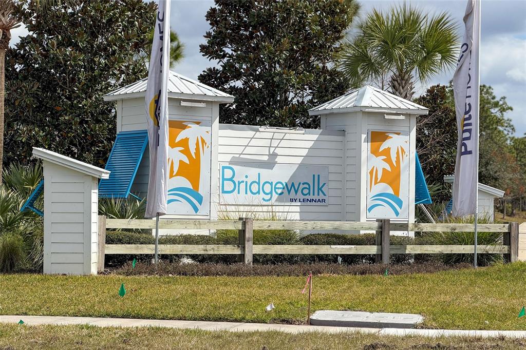 A white community entrance sign with palm tree graphics stands behind a wooden fence — 3040 PARK VALE ROAD, ST CLOUD, FL