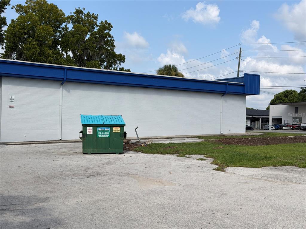 A green dumpster sits on a paved lot beside a white building with blue trim — 5920 SE HAMES ROAD, BELLEVIEW, FL