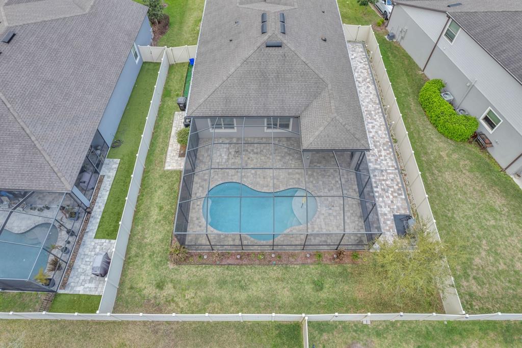 An aerial view shows a house with a screened-in pool and paver patio in the backyard — 12653 PALAPA LOOP, SPRING HILL, FL