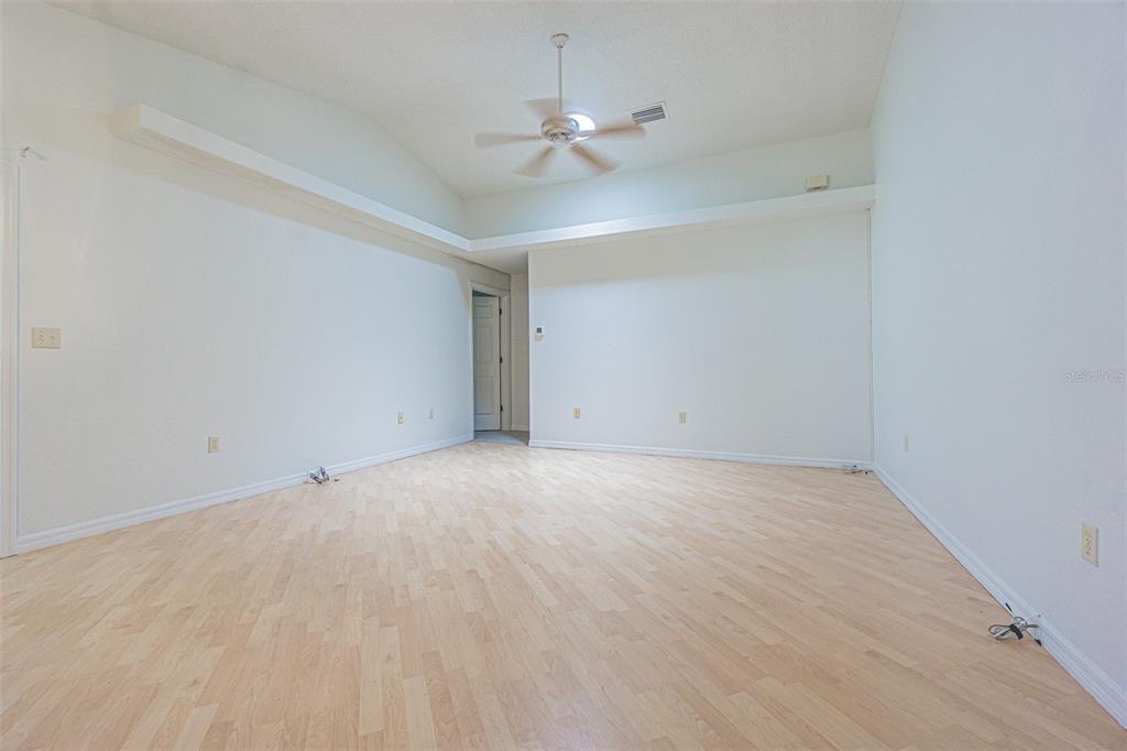 An empty room features light wood flooring, white walls, a vaulted ceiling, and a ceiling fan — 8157 STURBRIDGE COURT, WEEKI WACHEE, FL