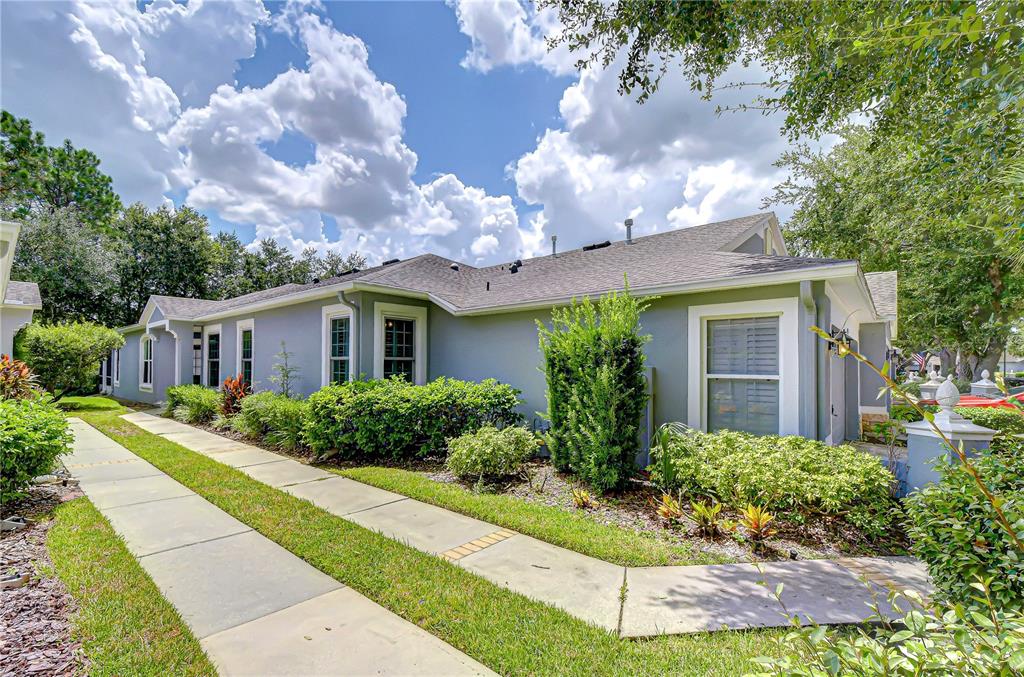 A gray house exterior with a concrete walkway, green landscaping, and a blue sky — 6026 SANDHILL RIDGE DRIVE, LITHIA, FL