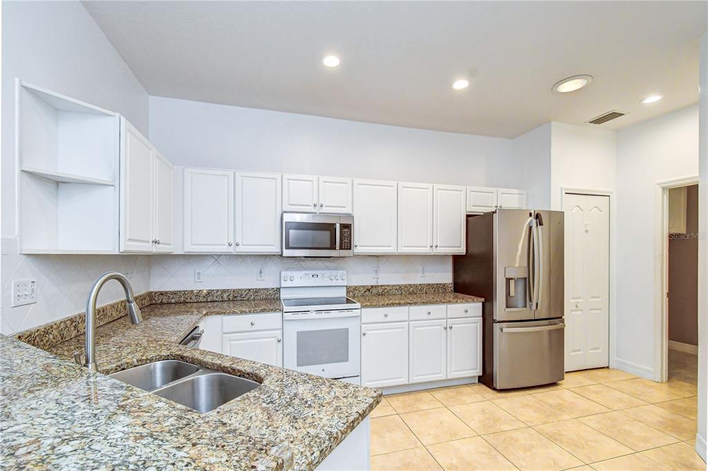 A kitchen with white cabinets, granite countertops, and stainless steel appliances opens to a dining area — 6026 SANDHILL RIDGE DRIVE, LITHIA, FL