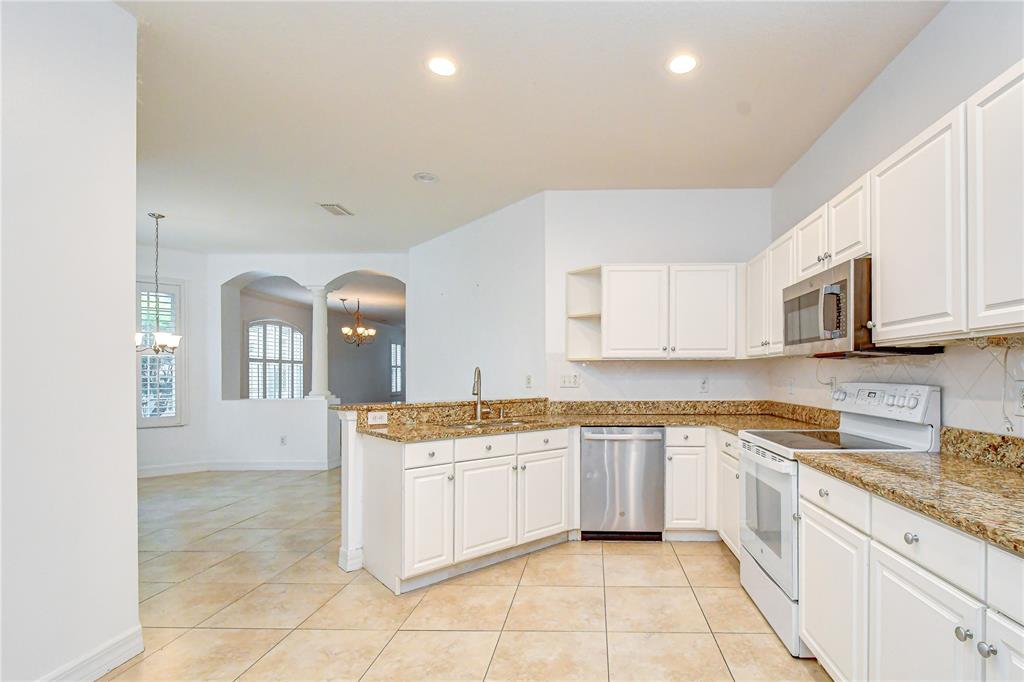 A kitchen with white cabinets, granite countertops, stainless steel appliances, and beige tile flooring — 6026 SANDHILL RIDGE DRIVE, LITHIA, FL