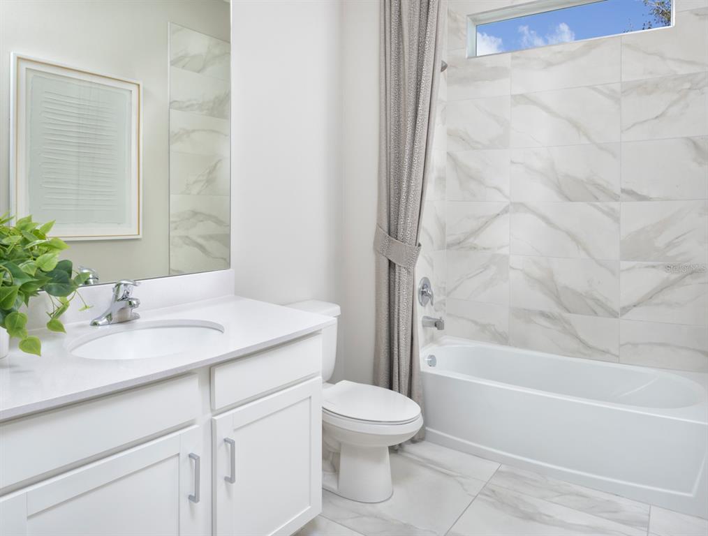 A bathroom features a white vanity, a toilet, and a bathtub with marble-look tile walls — 18501 VISTA PARK, VENICE, FL