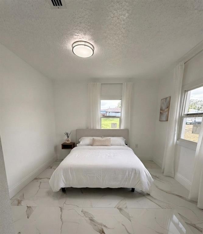 A bedroom features a bed, a floating nightstand, white walls, and white marble-look tile flooring — 5228 ANDRUS AVENUE, ORLANDO, FL