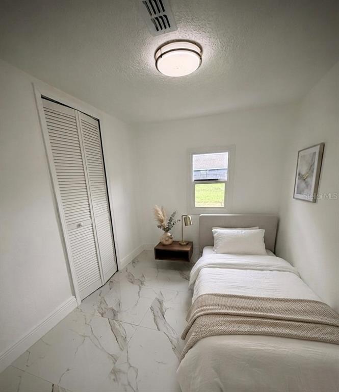 A small bedroom features white walls, a single bed, a floating nightstand, and marble-patterned flooring — 5228 ANDRUS AVENUE, ORLANDO, FL