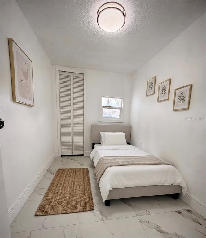 A small bedroom features a twin bed, white walls, tile flooring, and a louvered closet door — 5228 ANDRUS AVENUE, ORLANDO, FL