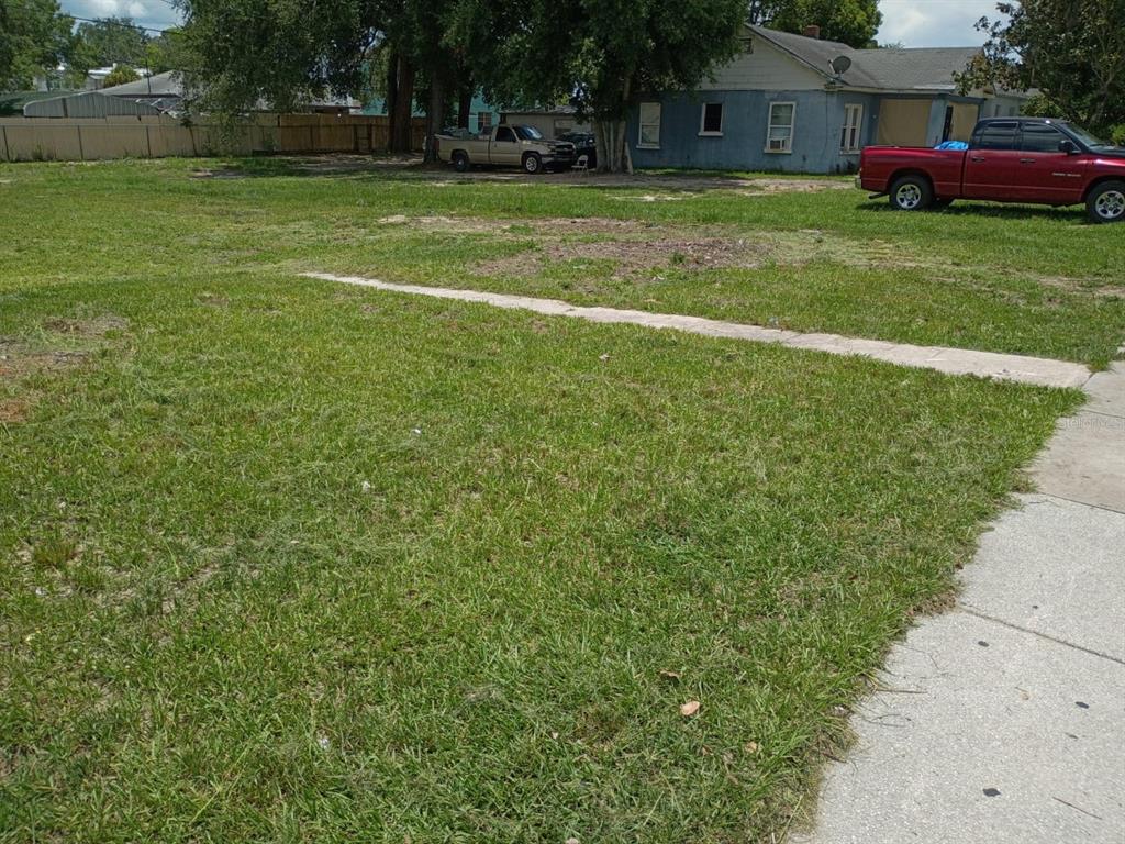 A grassy vacant lot sits in front of a blue house and a red pickup truck — 15 W SESSOMS AVENUE, LAKE WALES, FL