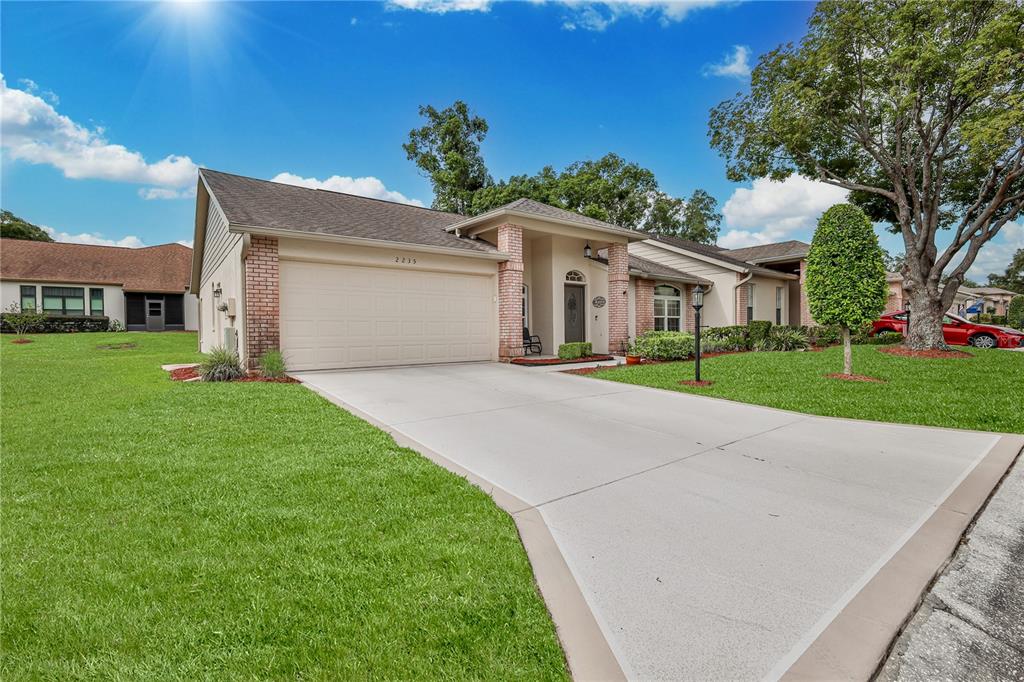 A single-story suburban house with a beige exterior, brick accents, and a concrete driveway — 2235 SPRINGMEADOW DRIVE, SPRING HILL, FL