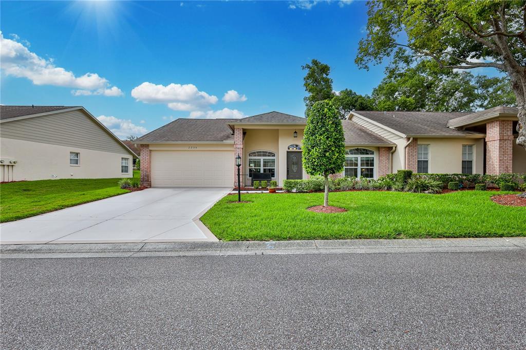 A single-story house with a beige exterior, a two-car garage, and a manicured front lawn — 2235 SPRINGMEADOW DRIVE, SPRING HILL, FL