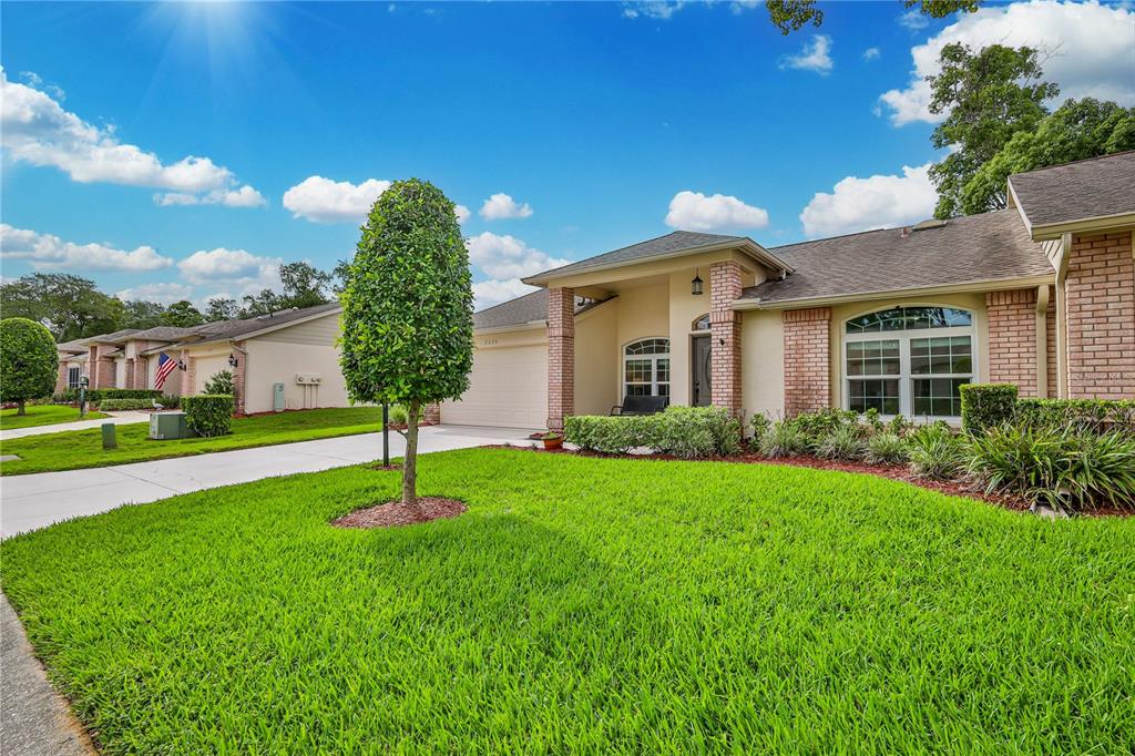 A single-story brick and stucco house with a manicured lawn and a paved driveway — 2235 SPRINGMEADOW DRIVE, SPRING HILL, FL