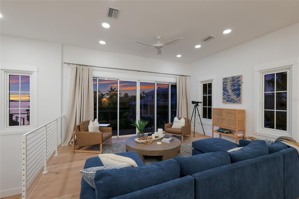 A living room features a blue sectional, two leather chairs, and large windows overlooking water — 511 59TH STREET, BRADENTON BEACH, FL