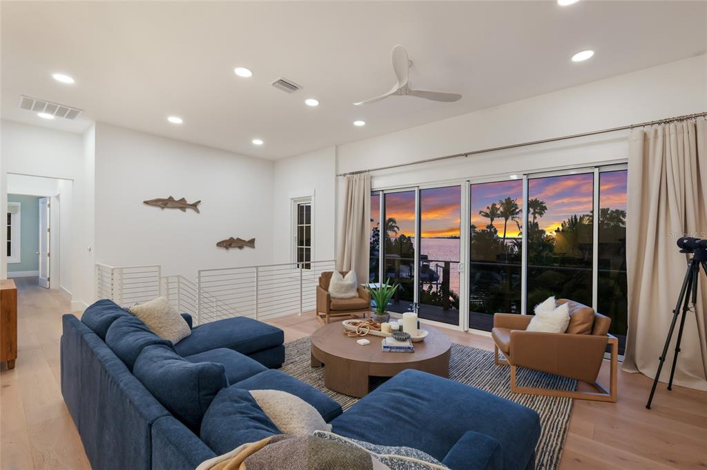 A living room features a blue sectional, leather chairs, and sliding doors overlooking a sunset — 511 59TH STREET, BRADENTON BEACH, FL