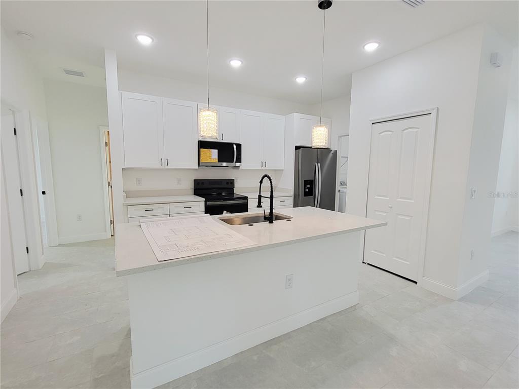 A modern kitchen features white cabinets, a central island with a dishwasher, and tile flooring — 415 TONKLIN ROAD SW, PALM BAY, FL