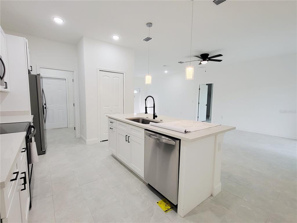 An open-concept kitchen and living area featuring white cabinets, stainless appliances, and tile flooring — 415 TONKLIN ROAD SW, PALM BAY, FL