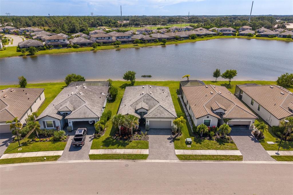 An aerial view shows three suburban houses with tiled roofs situated along a lake — 13845 PINE LODGE LANE, FORT MYERS, FL