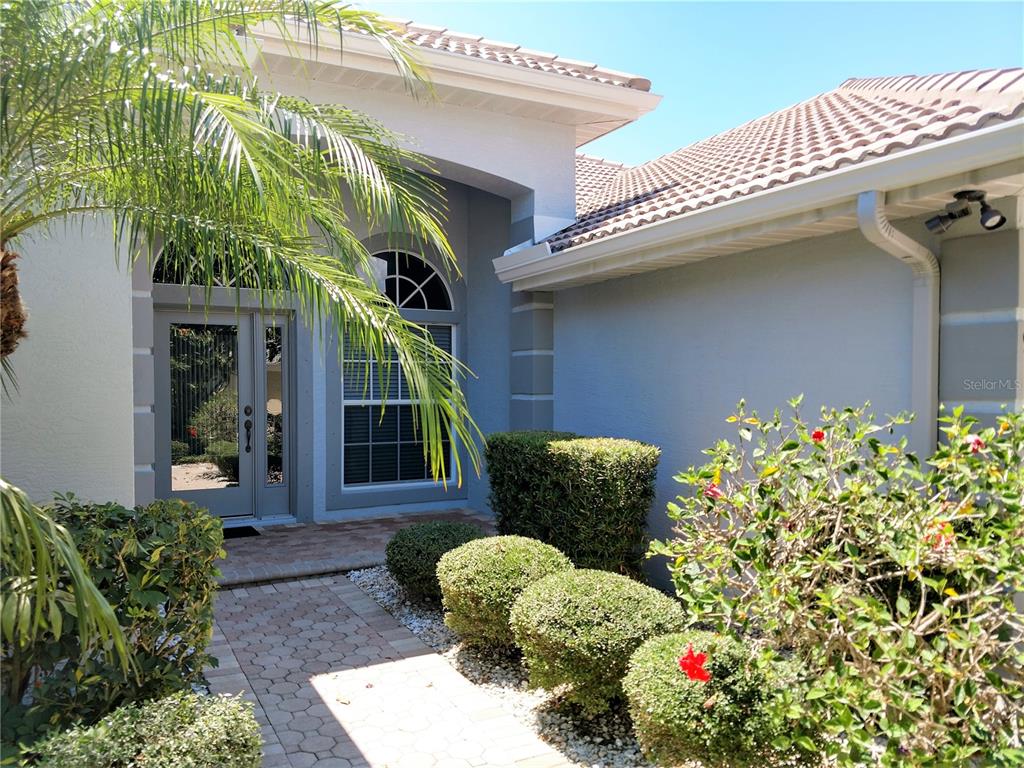 The exterior of a house features a paved walkway, manicured shrubs, and a glass front door — 919 SCHERER WAY, OSPREY, FL