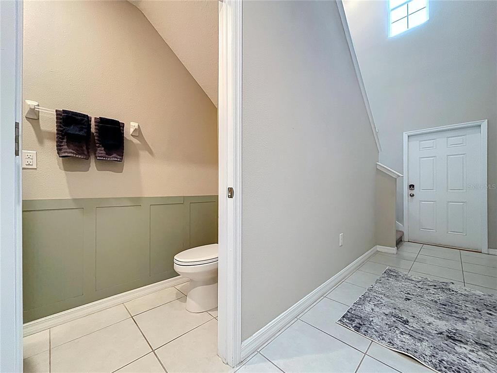 A small bathroom with green wainscoting and a toilet sits beside a tiled entryway — 3141 OYSTER COVE STREET, WIMAUMA, FL