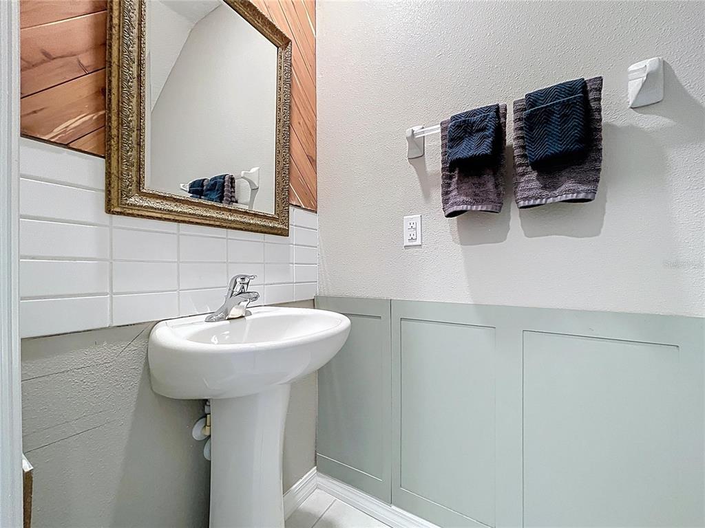 A bathroom features a pedestal sink, a framed mirror, subway tile, and light green wainscoting — 3141 OYSTER COVE STREET, WIMAUMA, FL