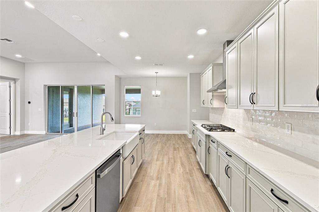 A modern kitchen features a large quartz island, white cabinetry, and light wood-look flooring — 3177 WOLF LAKE AVENUE, APOPKA, FL