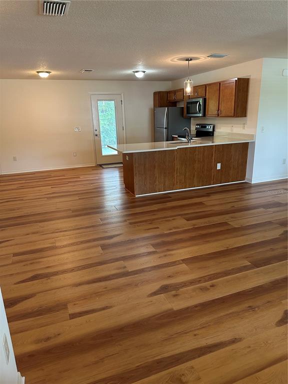 A kitchen features a white countertop island with a sink, wooden cabinets, and pendant lighting — 716 TRUMAN AVENUE, LADY LAKE, FL