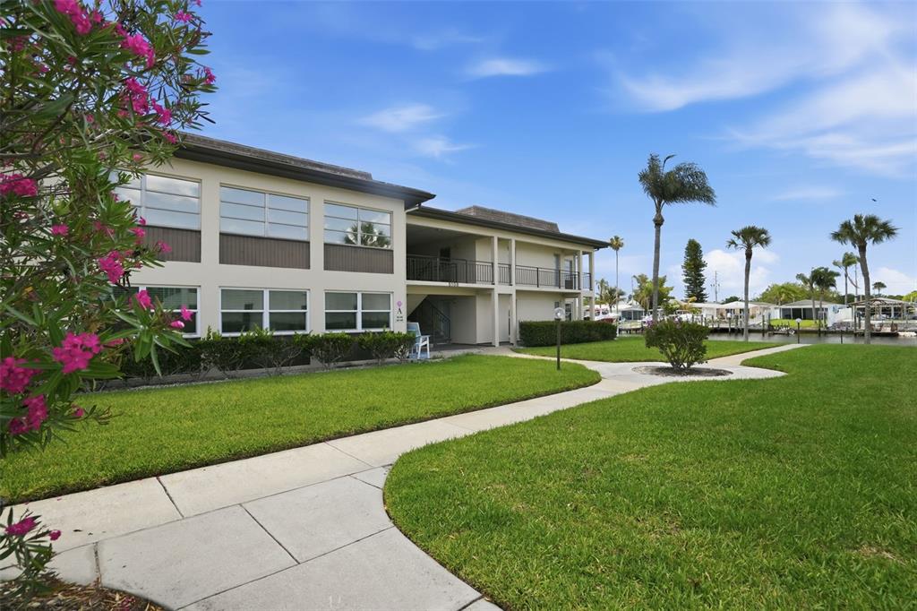 An exterior view of a multi-story apartment building situated along a canal with landscaping — 5108 AMULET DRIVE UNIT 205, NEW PORT RICHEY, FL